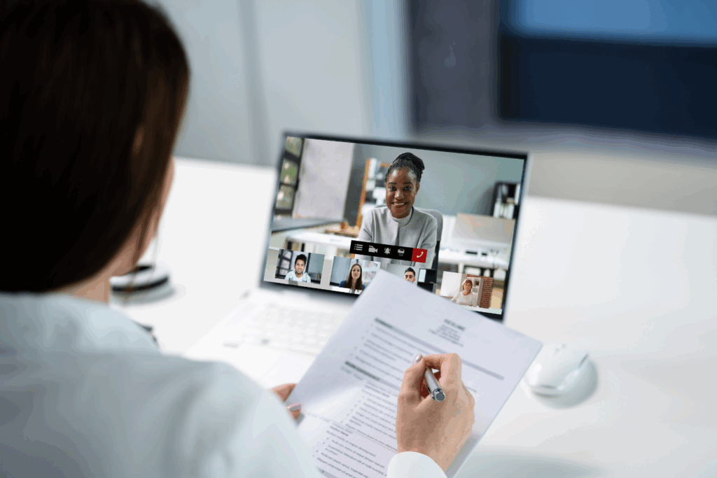 A hiring manager conducting a remote video interview with multiple candidates, reviewing a printed resume during the call. The image illustrates the process of remote hiring and virtual recruitment, supporting the blog’s theme of accessing global talent through digital platforms.
